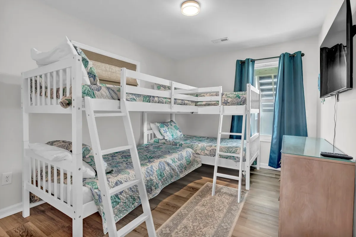 A whimsical bunk room with twin-over-twin bunk beds, textured bedding, and a window with curtains. The playful yet cozy atmosphere invites both children and adults to relax, play, or enjoy late-night conversations.