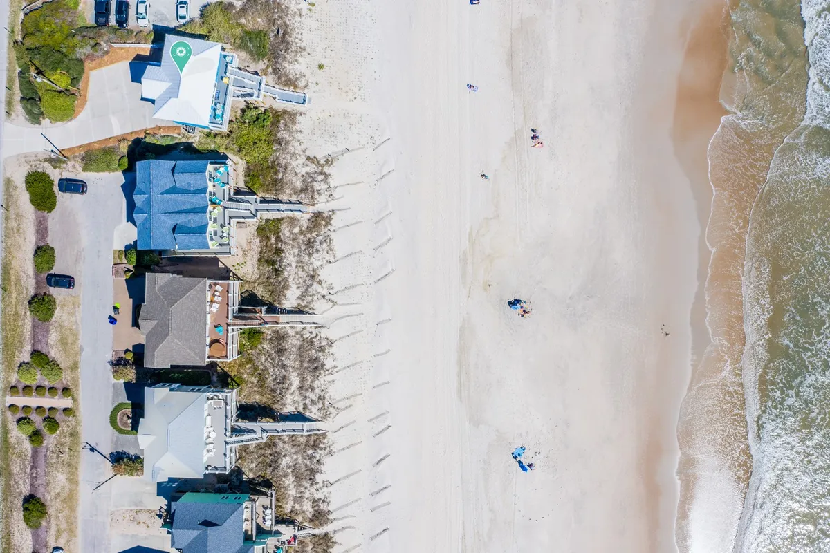A vibrant scene of beachfront houses with people enjoying the sandy beach and waves. This image captures the carefree spirit of summer with activities like sunbathing, swimming, and walking along the shore, framed by a lively coastal environment.
