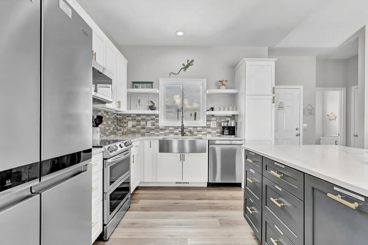 A stylish, contemporary kitchen with stainless steel Samsung appliances, a spacious kitchen island, crisp white cabinetry, and a large window offering picturesque views—potentially of the water. The setup encourages both gourmet cooking and social gatherings.