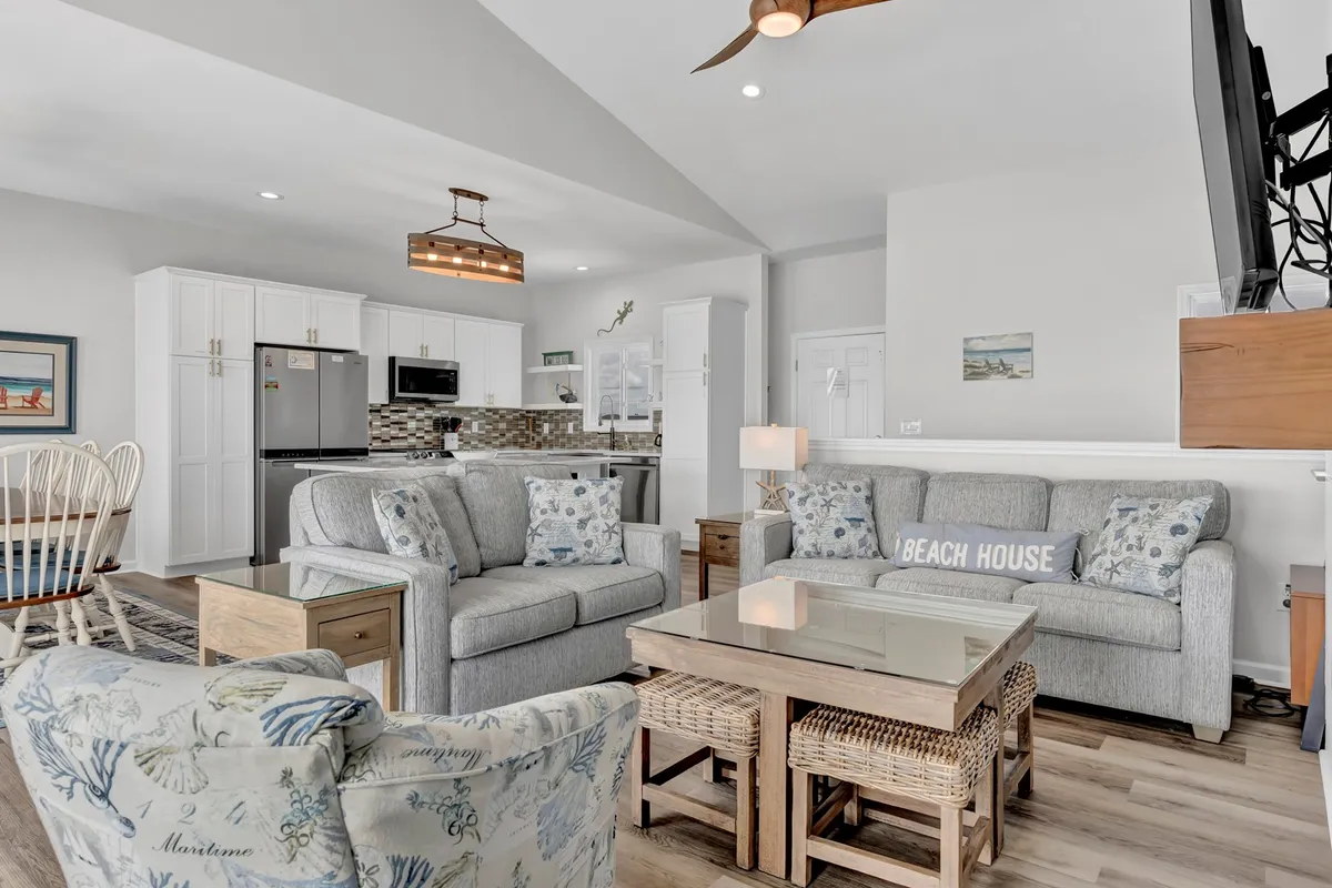 A spacious open-concept living area featuring comfortable seating arranged to enjoy both conversation and the panoramic view through large windows. The space elegantly bridges the living and dining zones, exuding a welcoming, family-friendly vibe. Beach-themed decor adds a touch of coastal charm, while the arrangement is clearly designed for socializing, relaxation, and gatherings.