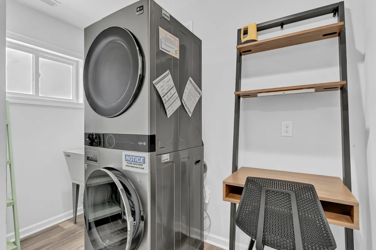 A tidy laundry room with a washer and dryer unit, shelving for organization, and a desk with chair. The utility sink is visible, emphasizing function and convenience for guests managing chores or cleaning up after beach or pet adventures.