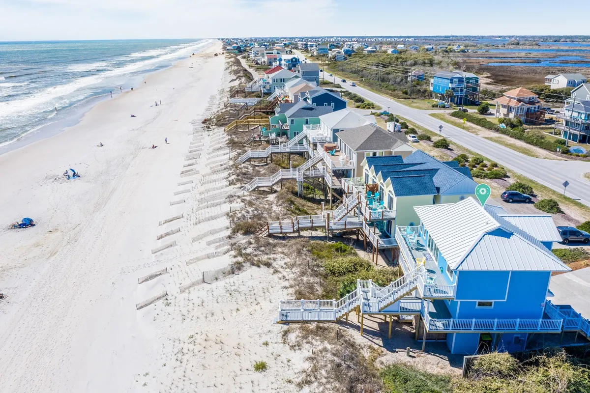 A wide sandy beach stretches in front of colorful beachfront houses, with boardwalks and open space ideal for gentle walks. The scene is lively and inviting, showing the proximity to accessible natural attractions and local amenities.