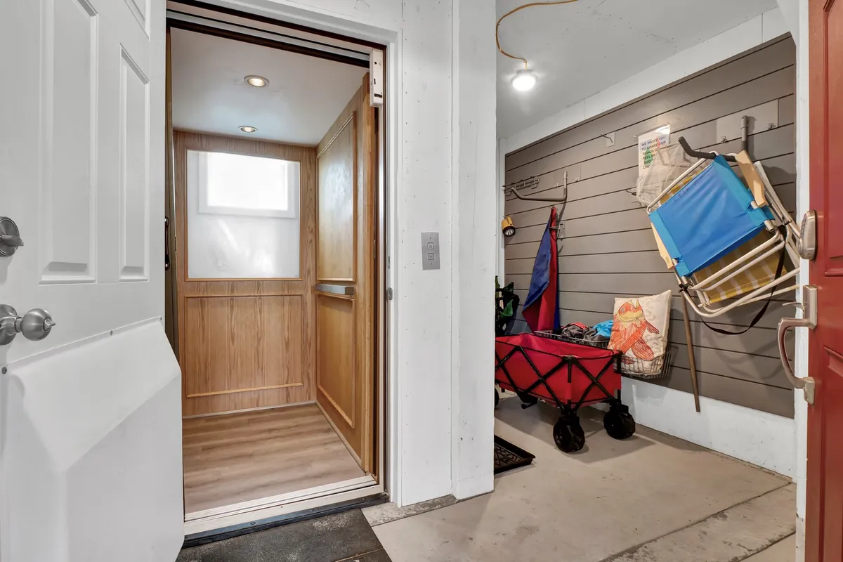 Inside the elevator room, the scene features a modern elevator with wood paneling and neatly organized beach toys and outdoor gear in storage compartments. The space is practical and secure, designed for family convenience and fun.
