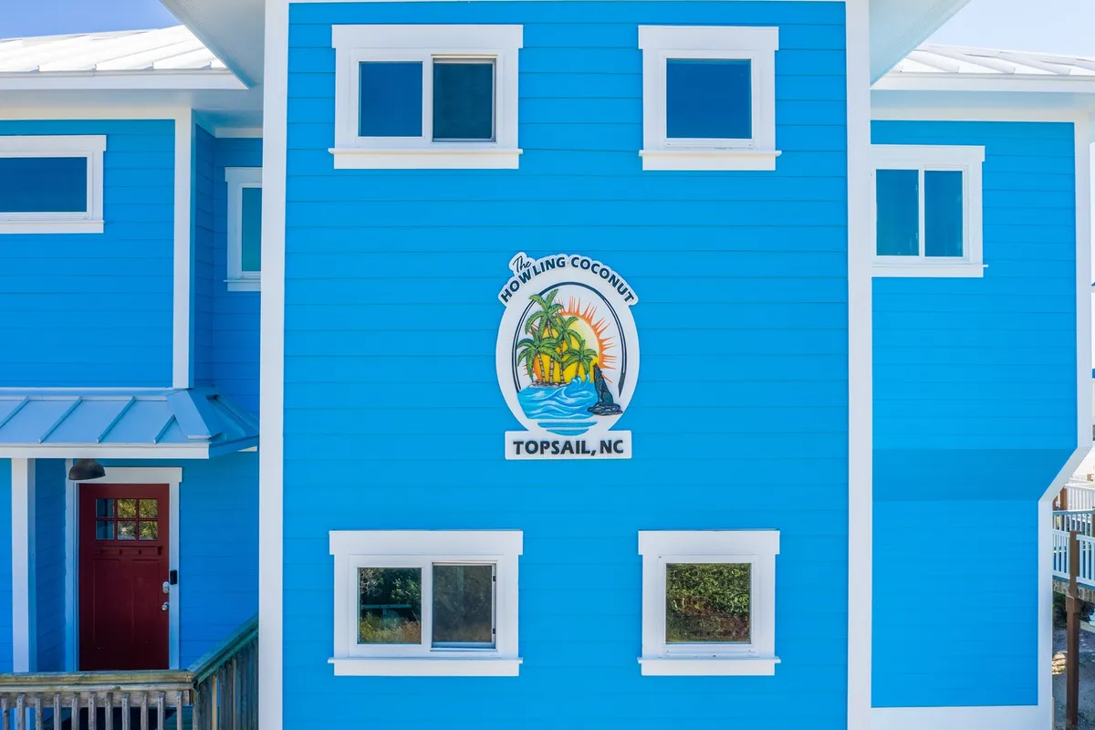 This image shows the vibrant blue house with a decorative palm tree sign, white trim, and a bold red door. The overall mood is playful and inviting, capturing the spirit of a fun, family- and pet-friendly getaway with beach activities nearby.